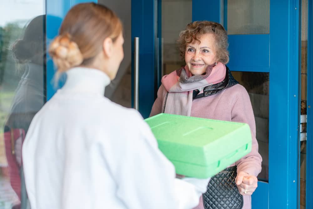 carer delivering meals on wheels to door of senior citizen